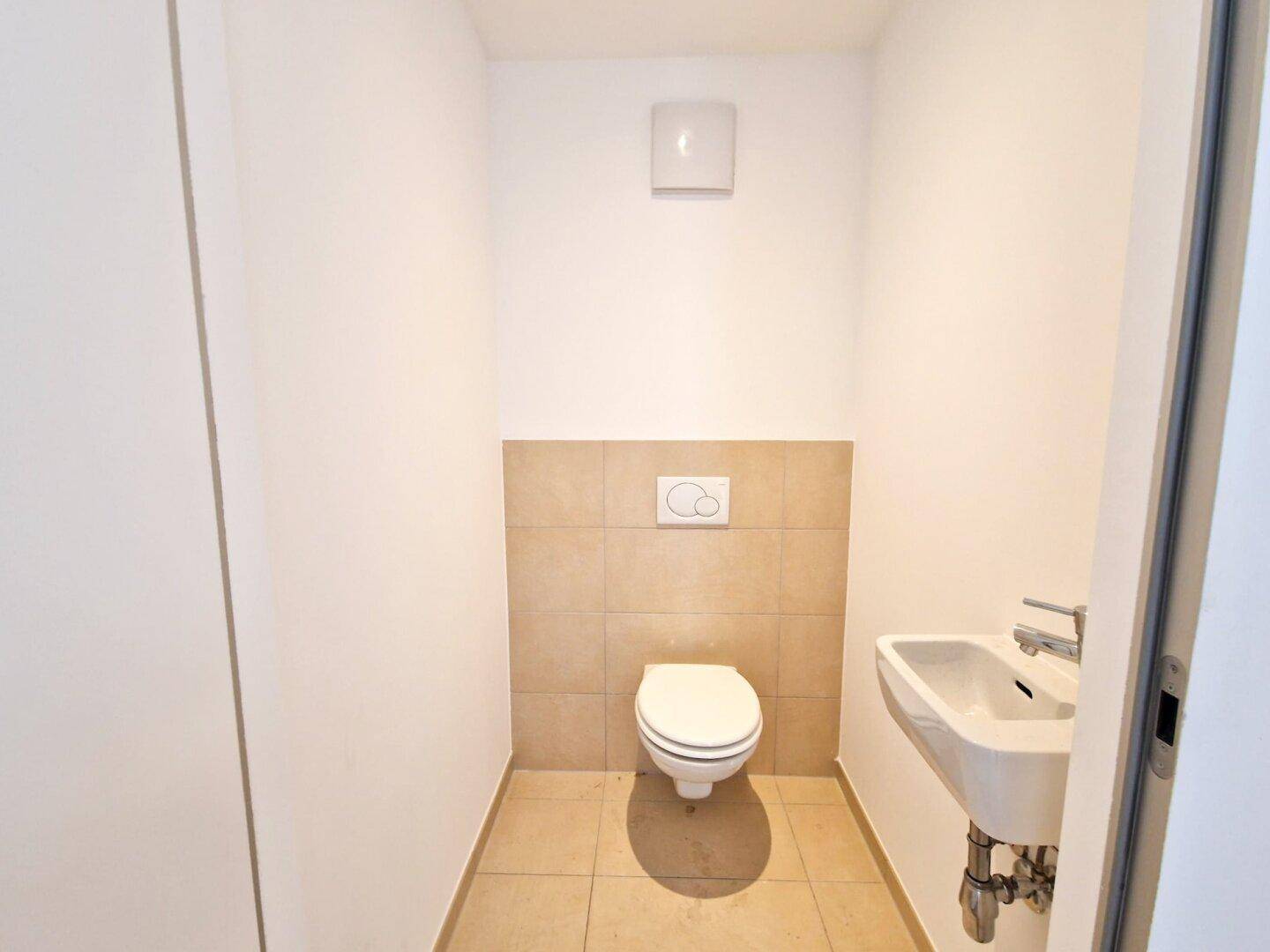 Kleines Gäste-WC mit Wand-WC, Waschbecken und Fliesenboden, praktisch und funktional gestaltet.