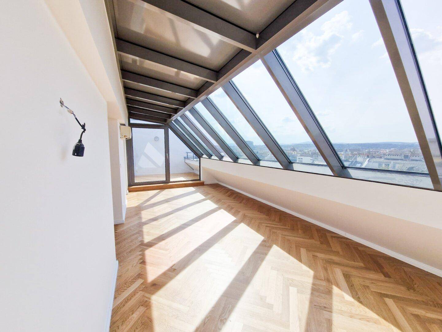 Geräumiger Wohnbereich mit hellem Fischgrätparkett und beeindruckendem Panoramablick durch die Schrägfenster.