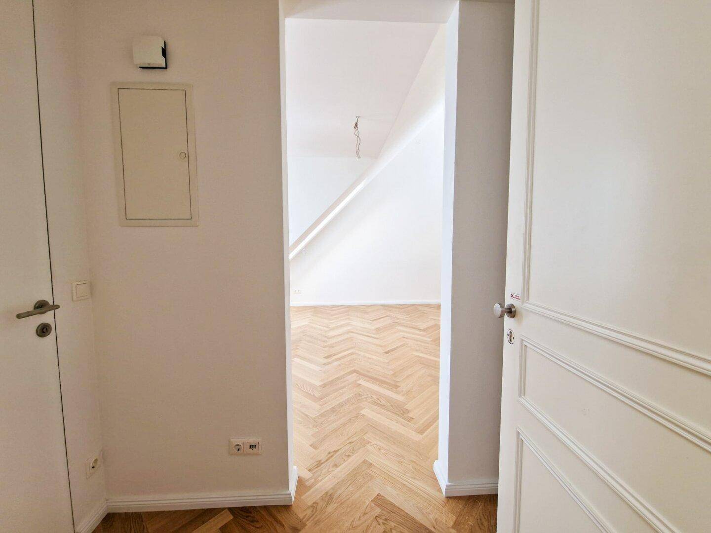 Heller Flur mit Fischgrätparkett, der den Blick in einen weiteren, lichtdurchfluteten Raum freigibt.