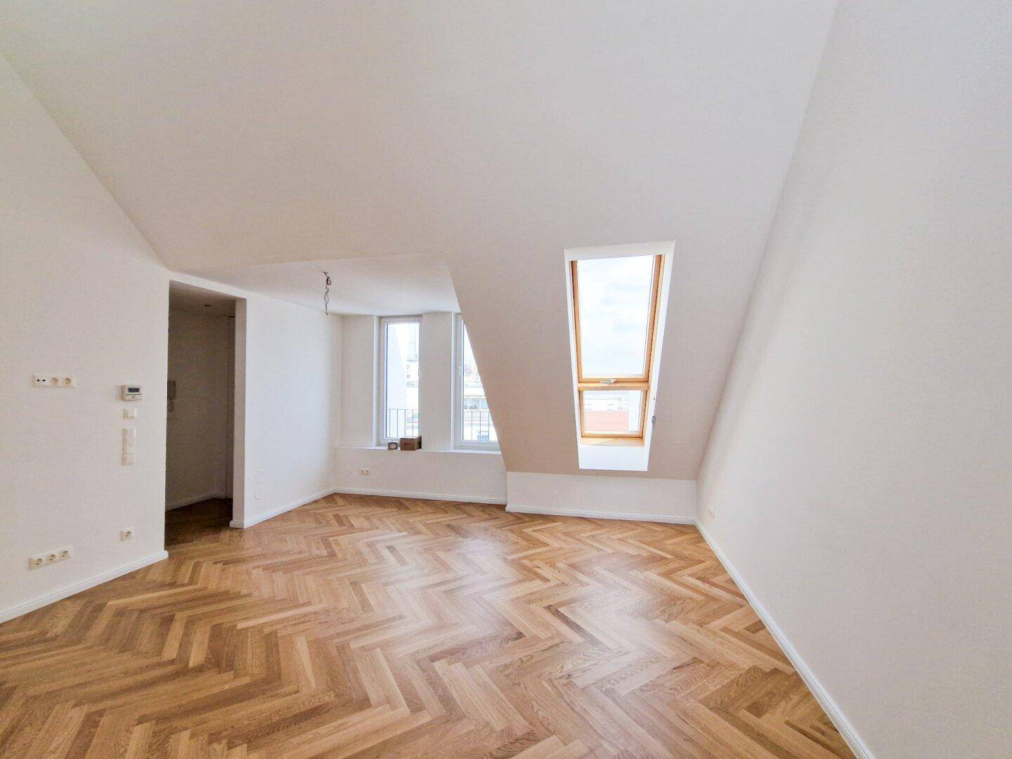 Heller Wohnbereich mit Fischgrätparkett, einem Fenster und einem zusätzlichen Dachfenster für optimale Belichtung.