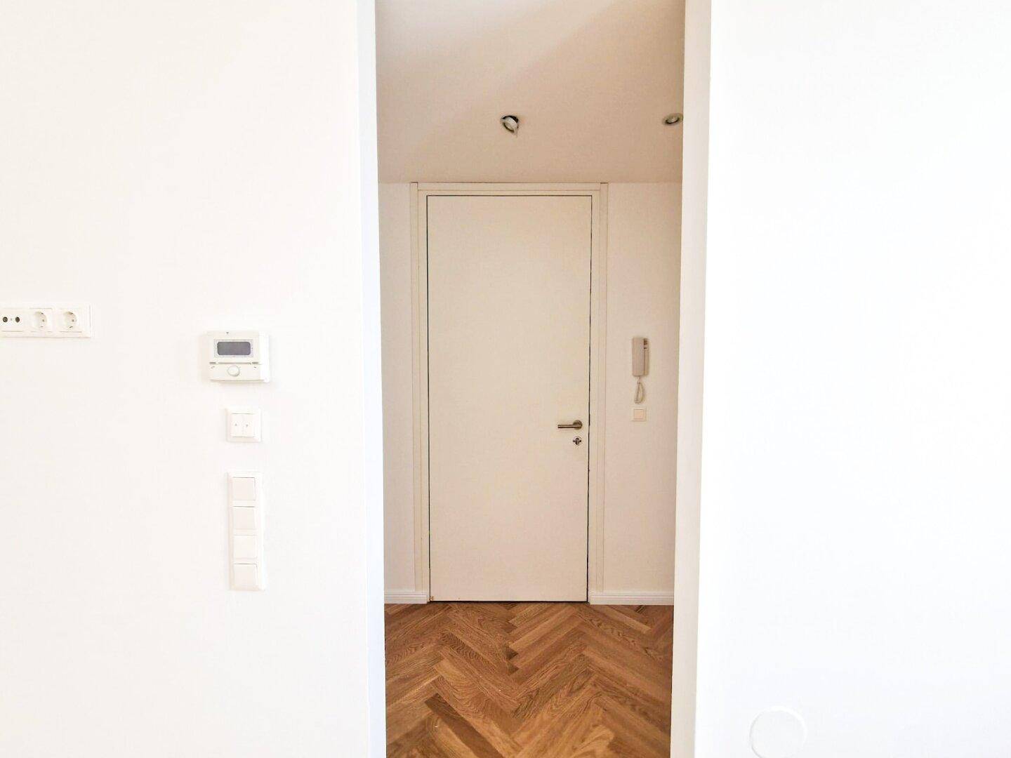 Heller Flur mit Fischgrätparkett und weißer Tür, die zu weiteren Wohnbereichen führt.