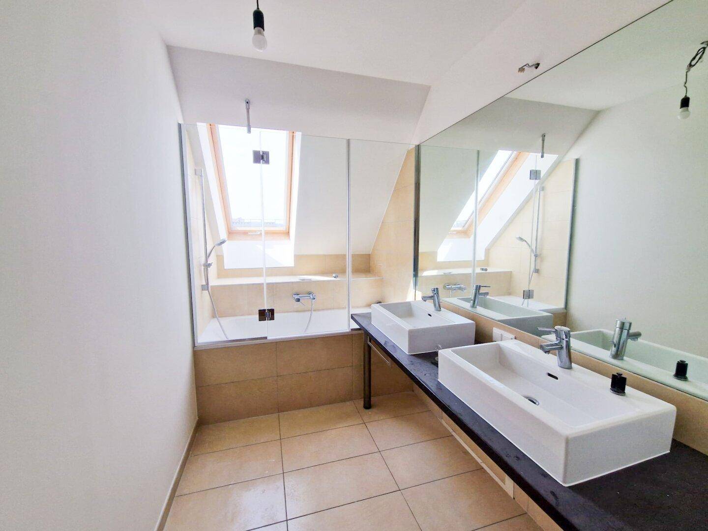 Modernes Badezimmer mit Doppelwaschbecken, Badewanne und Dachfenster für natürliche Belichtung.