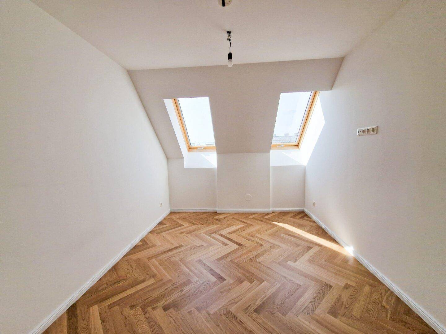 Geräumiges Zimmer mit Fischgrätparkett und Dachfenstern, das viel Tageslicht und eine angenehme Atmosphäre bietet.