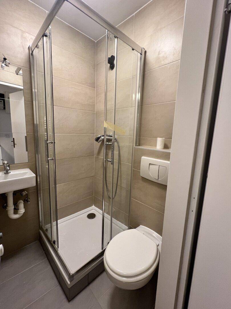 Kompaktes Badezimmer mit Duschkabine, WC und Einzelwaschbecken, ausgestattet mit hellen Wand- und Bodenfliesen.