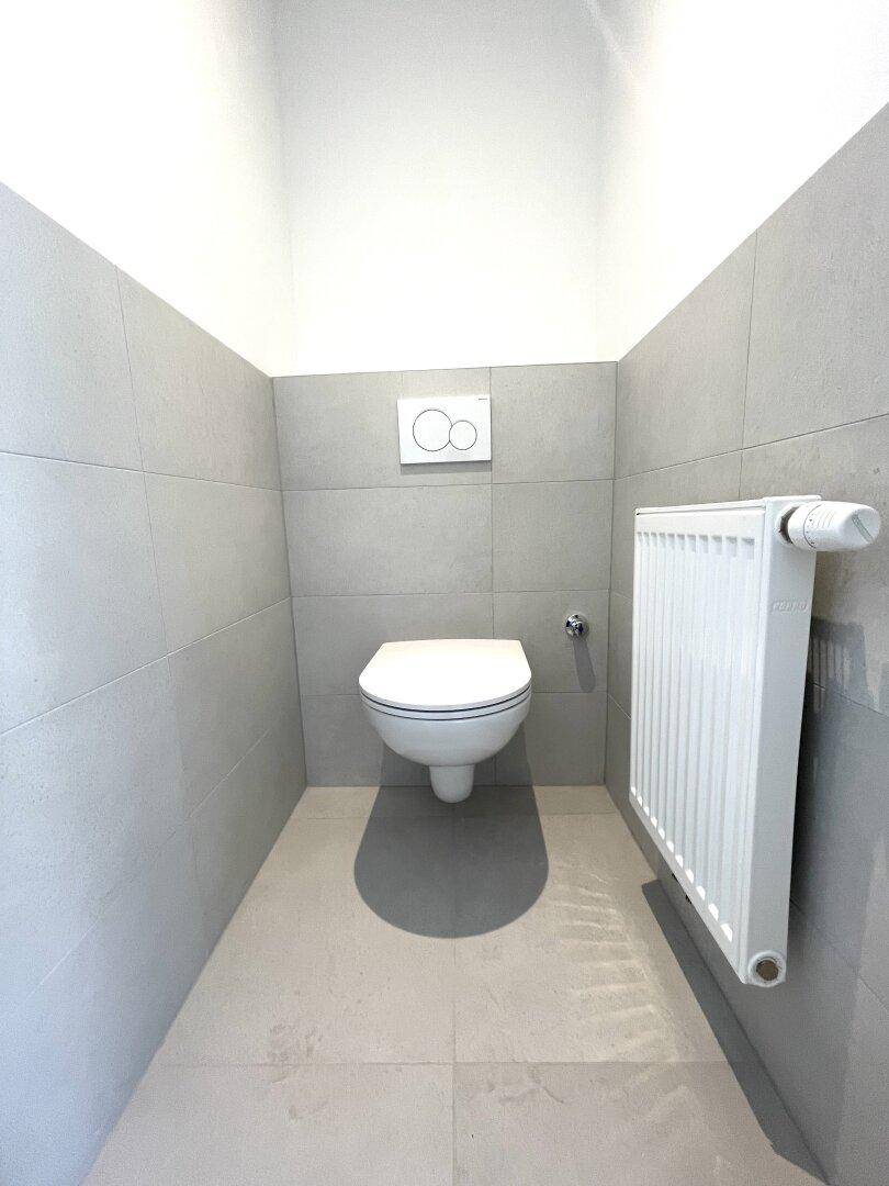 Separates WC mit wandhängender Toilette und modernen grauen Fliesen.
