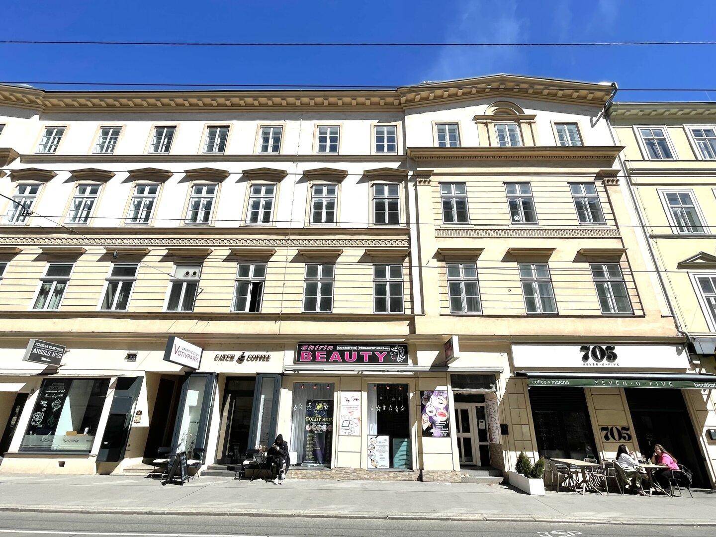 Klassische Stadtfassade mit mehreren Geschäften im Erdgeschoss und blauer Himmel.