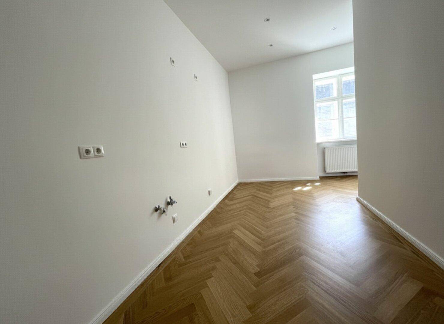 Leerer Raum mit Fischgrätparkett und Fenster, vorbereitet für individuelle Nutzung.