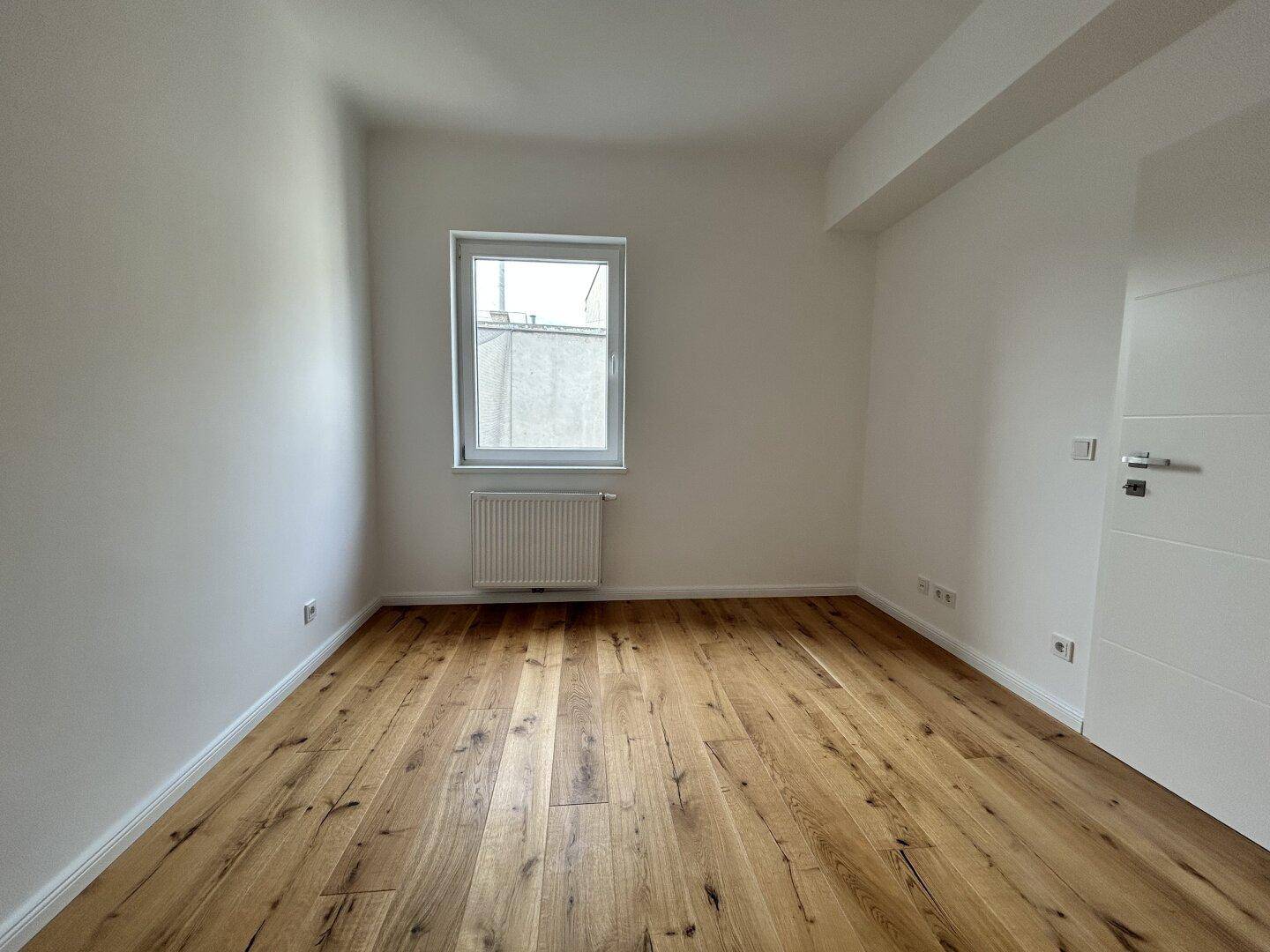 Kleineres, helles Zimmer mit Holzboden und einem Fenster, ideal als Schlaf- oder Arbeitszimmer.