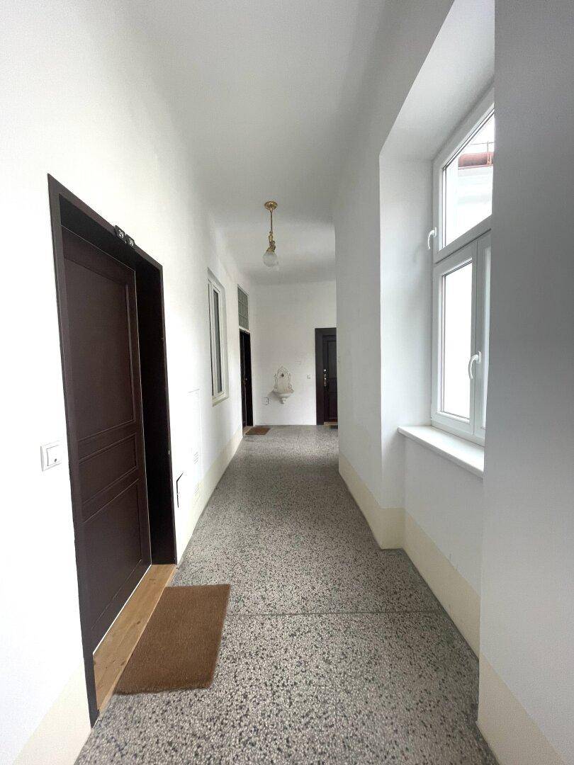Langer, heller Flur mit Terrazzoboden und mehreren Wohnungstüren in einem Altbau.