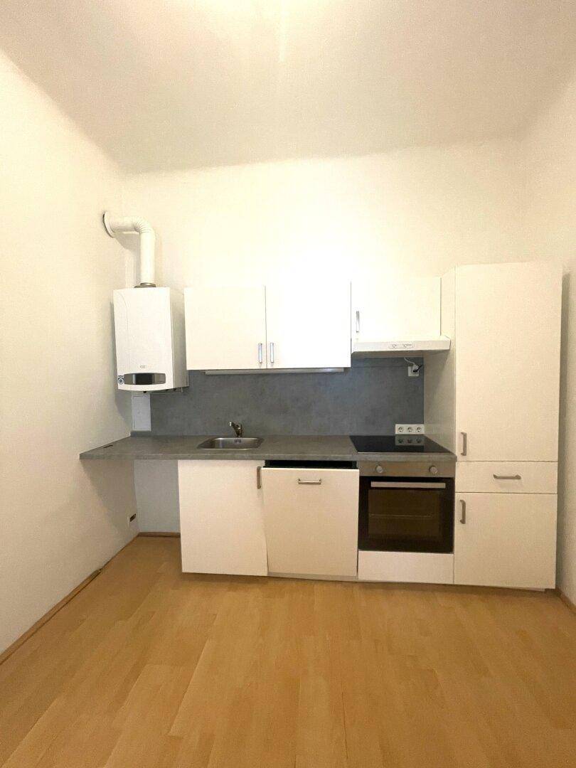 Kleine, moderne Einbauküche mit weißen Schränken, Kochfeld und Backofen in einem offenen Raum.