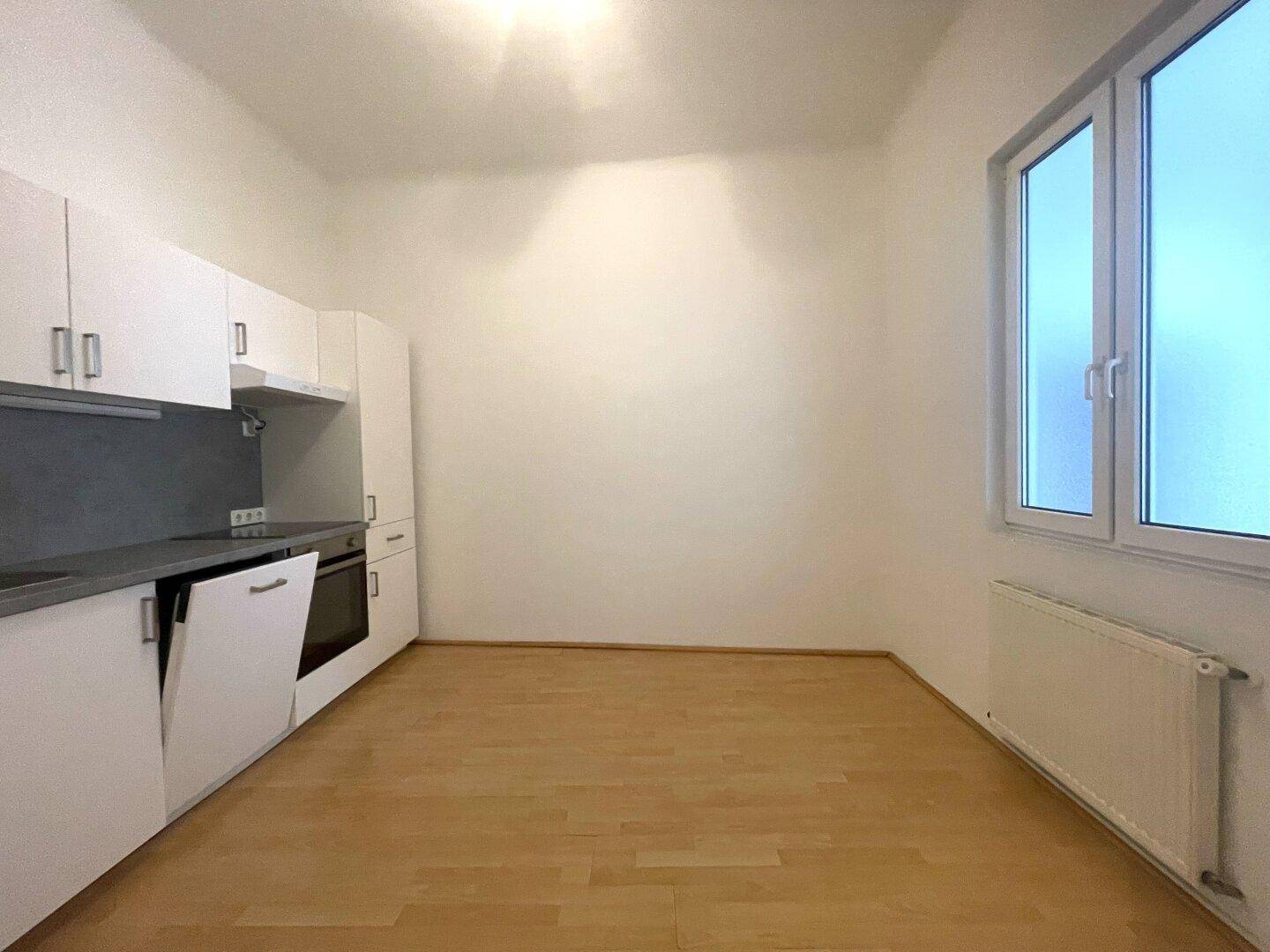 Heller Raum mit neuer Einbauküche, Holzfußboden und großem Fenster.