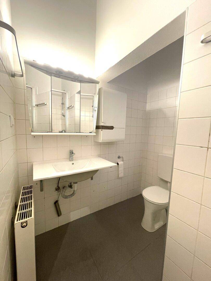 Modernes Badezimmer mit Dusche, WC, Waschbecken, Spiegelschrank und Handtuchheizkörper.