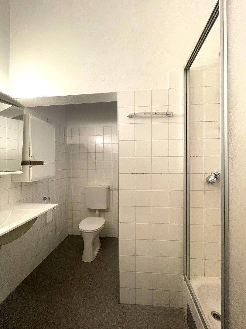 Helles Badezimmer mit Duschkabine, WC und weißen Fliesen.