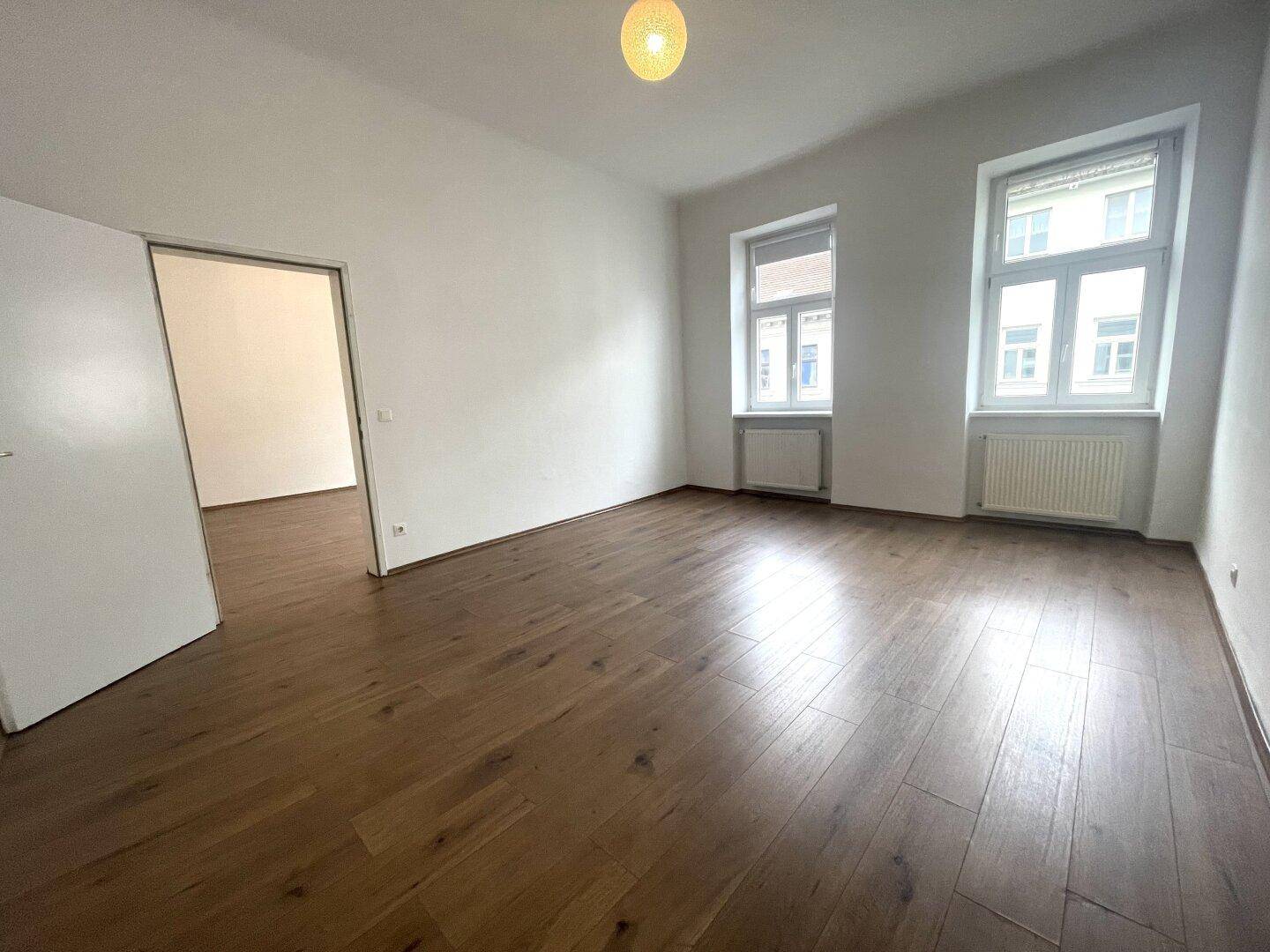 Heller Wohnraum mit Holzboden, hohen Decken und Blick auf die Stadt.
