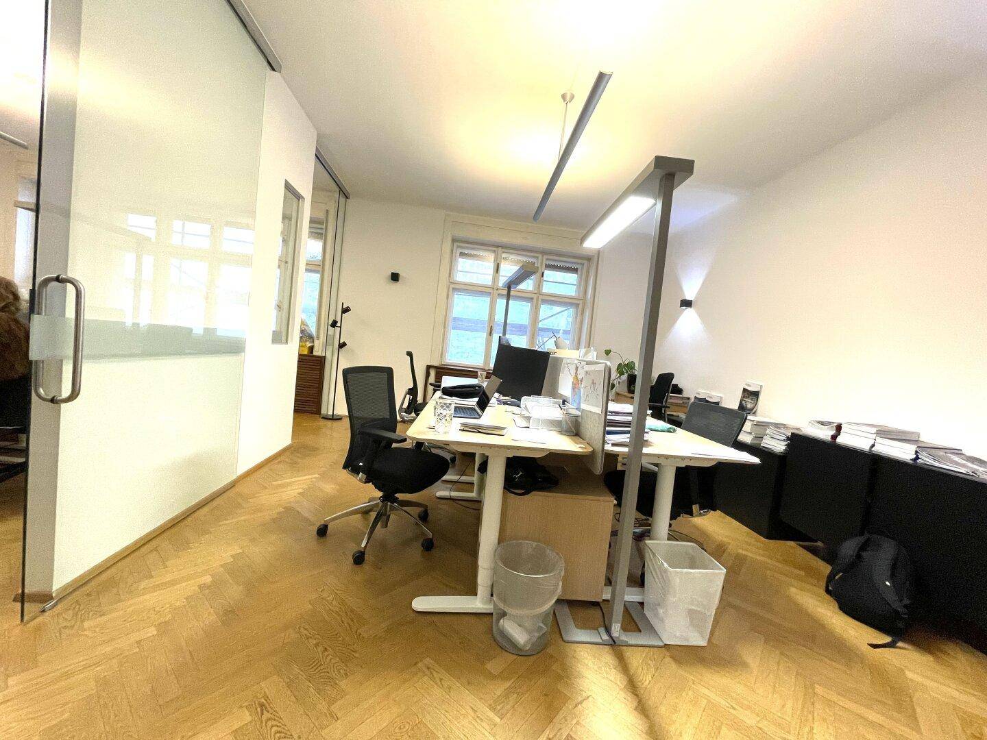 Helles Büro mit Glasabtrennung, Schreibtischen und klassischem Fischgrätparkett.