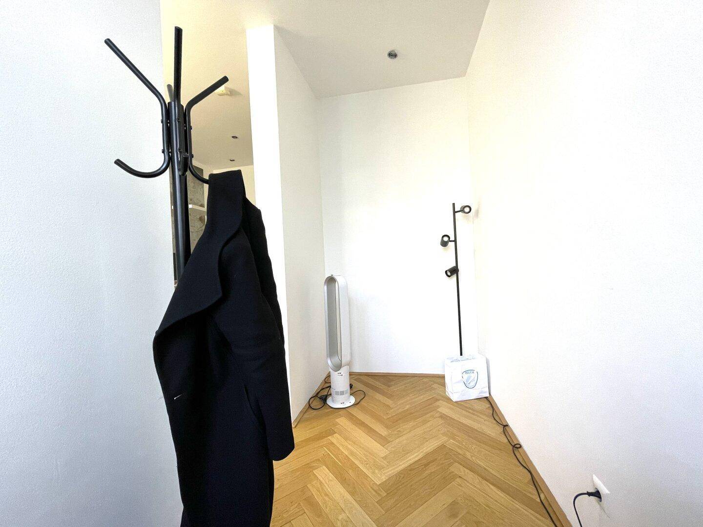 Heller Eingangsbereich mit Fischgrätparkett, Garderobe und einem modernen Ventilator.