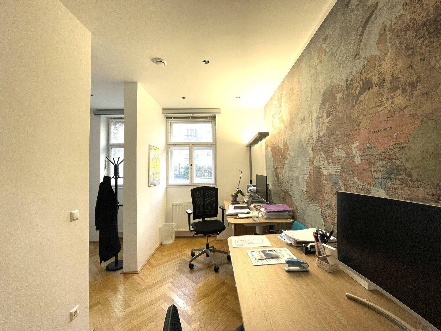 Büro mit Weltkarten-Tapete, Schreibtischen und einem Fenster mit Blick nach draußen.