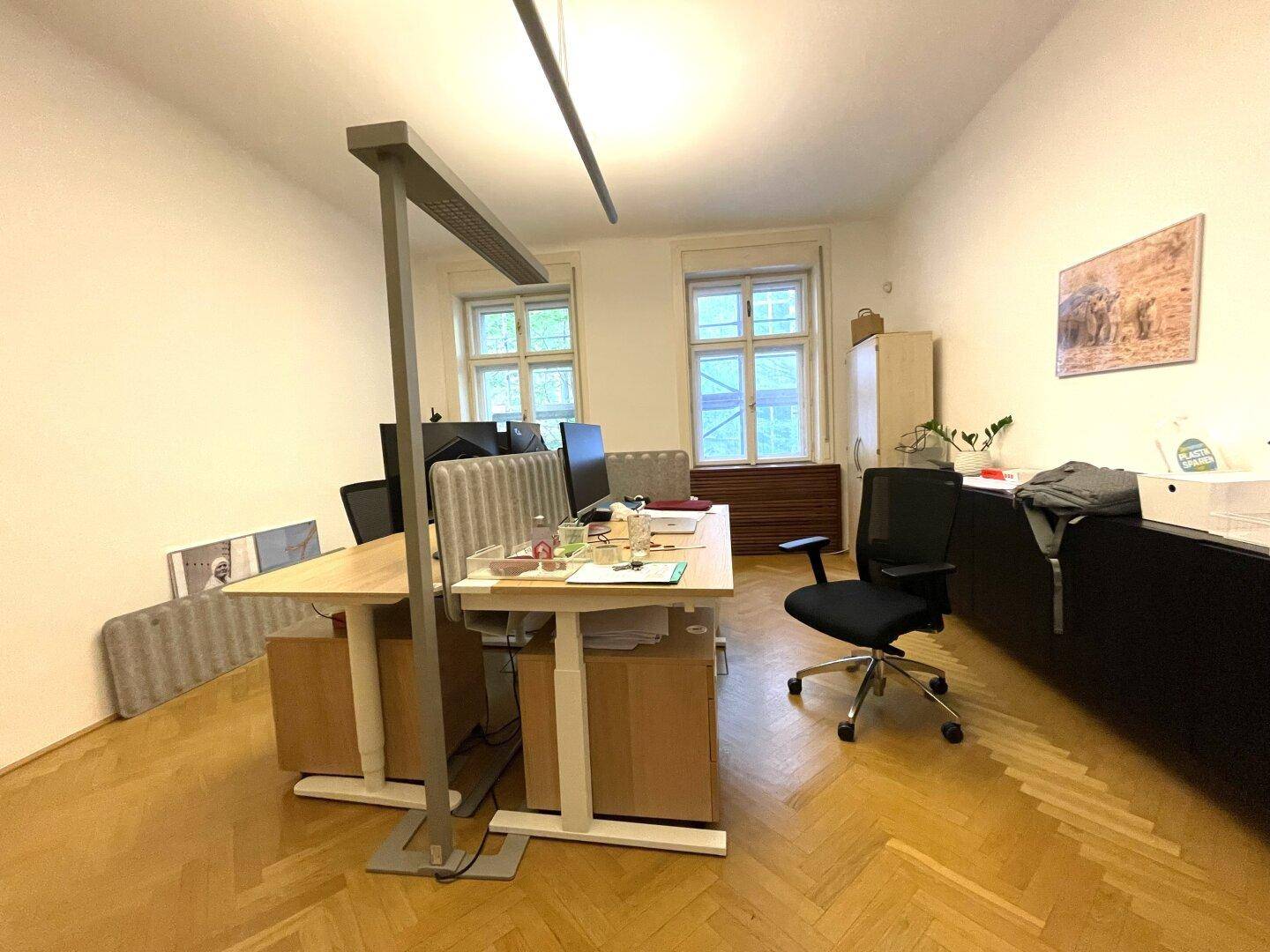 Geräumiges Büro mit zwei Arbeitsplätzen, großen Fenstern und hellem Fischgrätparkett.