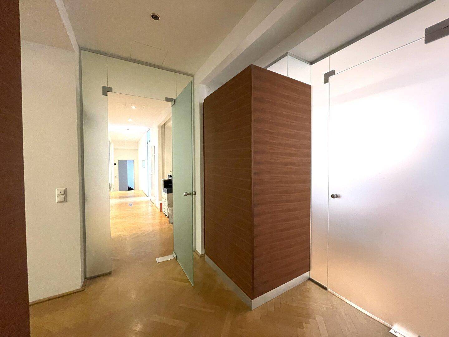 Heller Flur mit Fischgrätparkett, modernen Glastüren und einer Holzwandverkleidung.