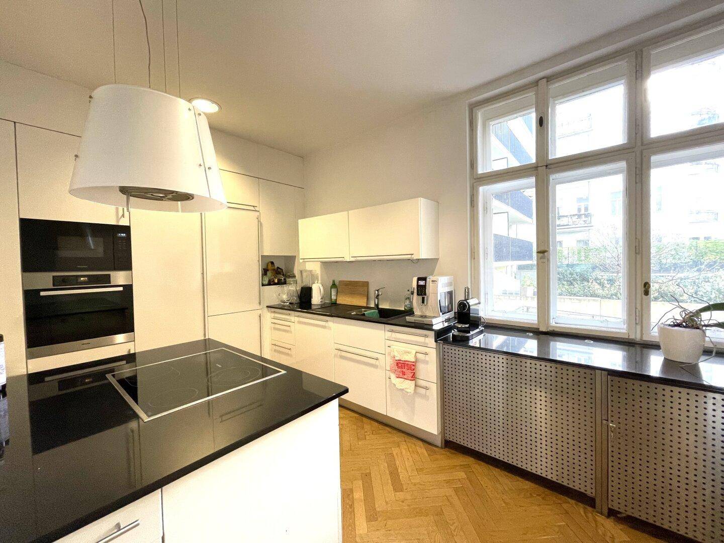 Moderne weiße Küche mit Kochinsel, schwarzen Arbeitsplatten und großen Fenstern.
