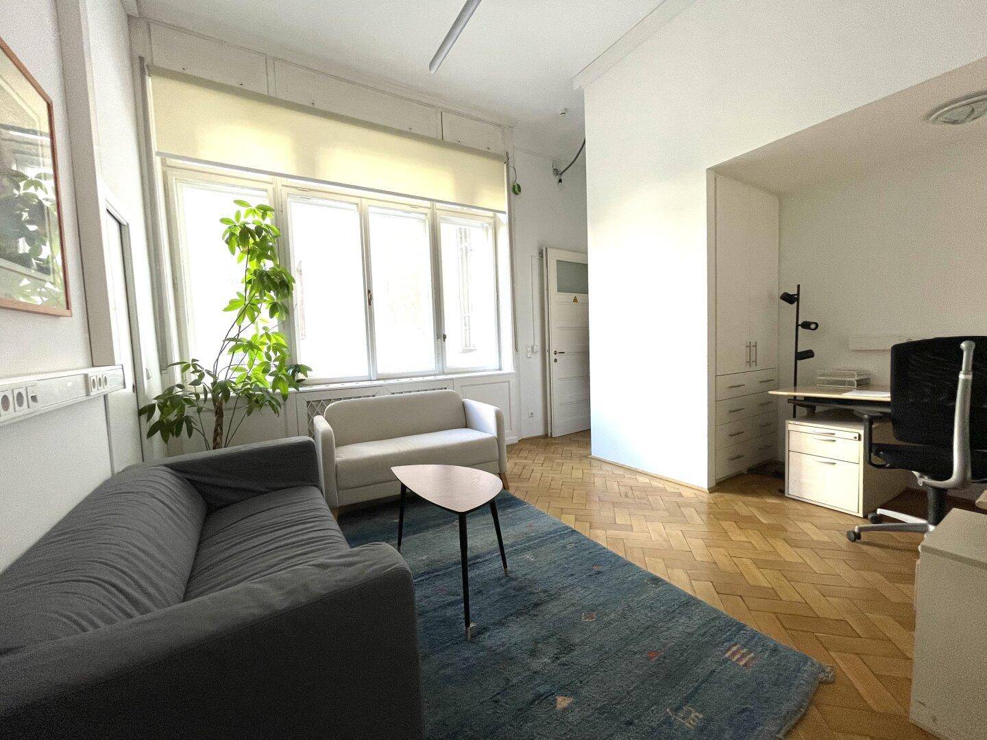 Büro mit Sitzbereich, großem Fenster und Schreibtisch, ausgestattet mit Fischgrätparkett.