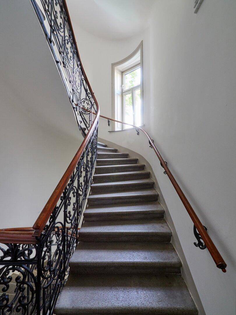 Elegantes Treppenhaus mit geschwungenem Geländer aus Schmiedeeisen und Holzhandlauf.