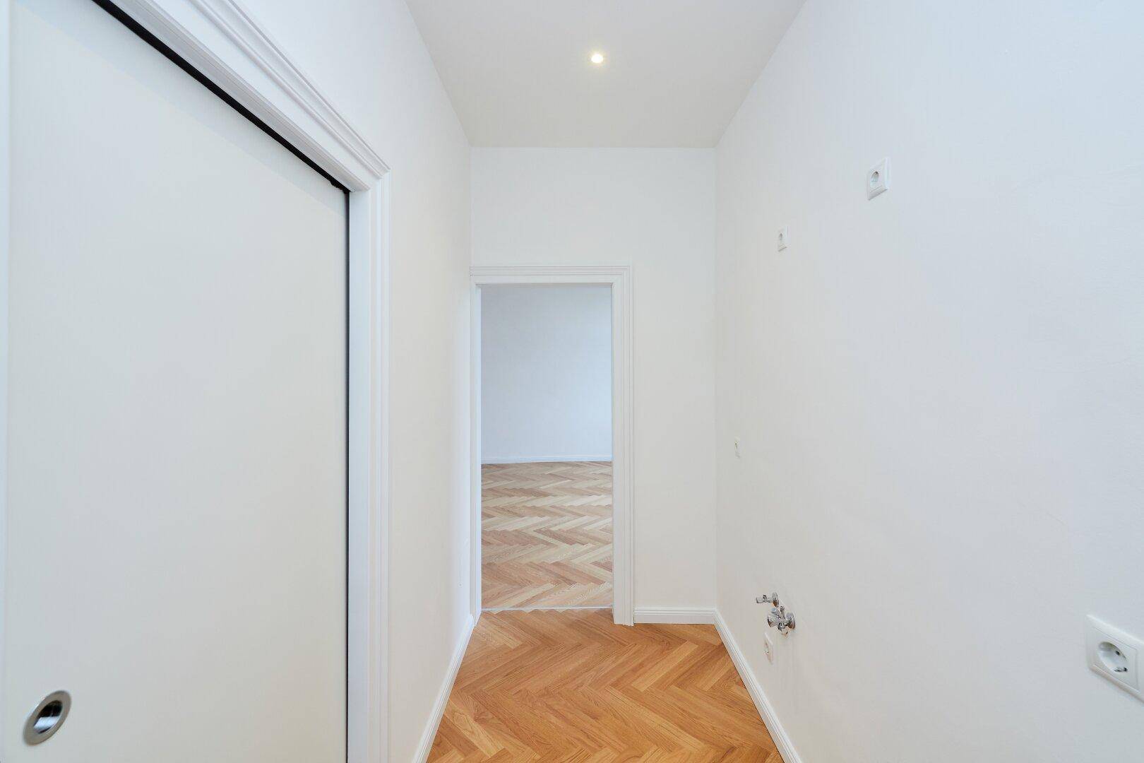 Heller Flur mit Fischgrätparkett und Zugang zu weiteren Räumen der Wohnung.