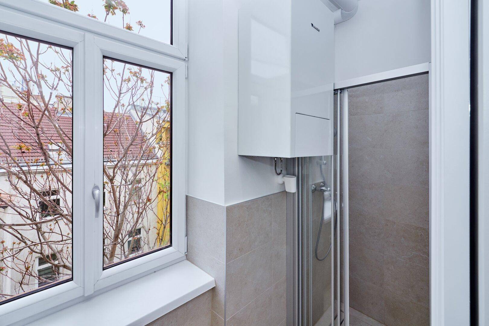 Kleines Badezimmer mit Duschkabine, Gastherme und Fenster für natürliche Belüftung.