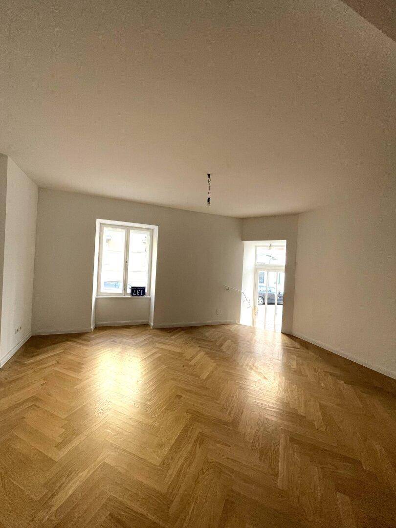 Heller Wohnraum mit Fischgrätparkett, großem Fenster und Blick auf die Straße.