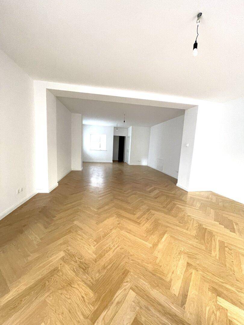 Weitläufiger Wohnbereich mit hellem Fischgrätparkett und weißen Wänden, ideal für offene Gestaltung.