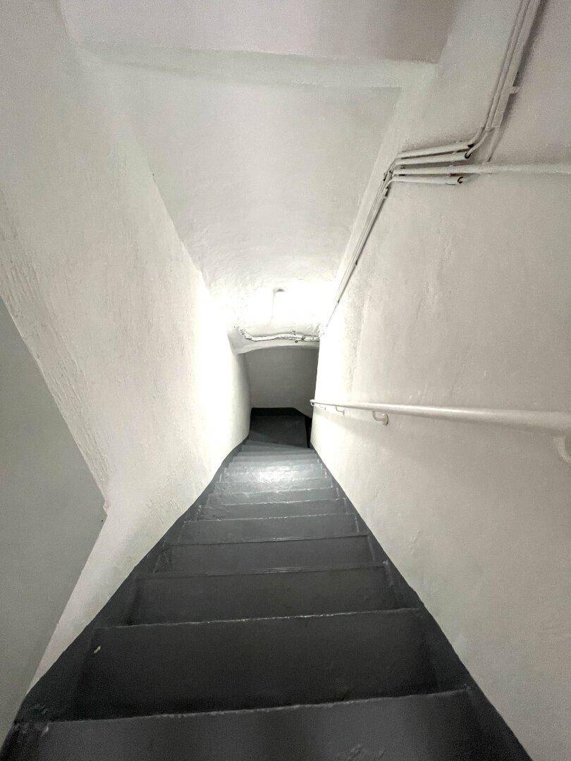 Schmaler Treppenabgang in den Keller mit weiß gestrichenen Wänden und Handlauf.