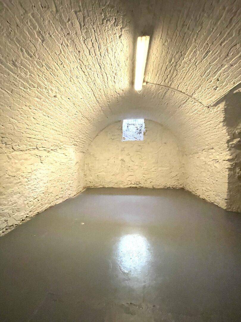 Gewölbekeller mit rauen, weiß gestrichenen Wänden und kleinem Fenster, ideal als Lagerraum.