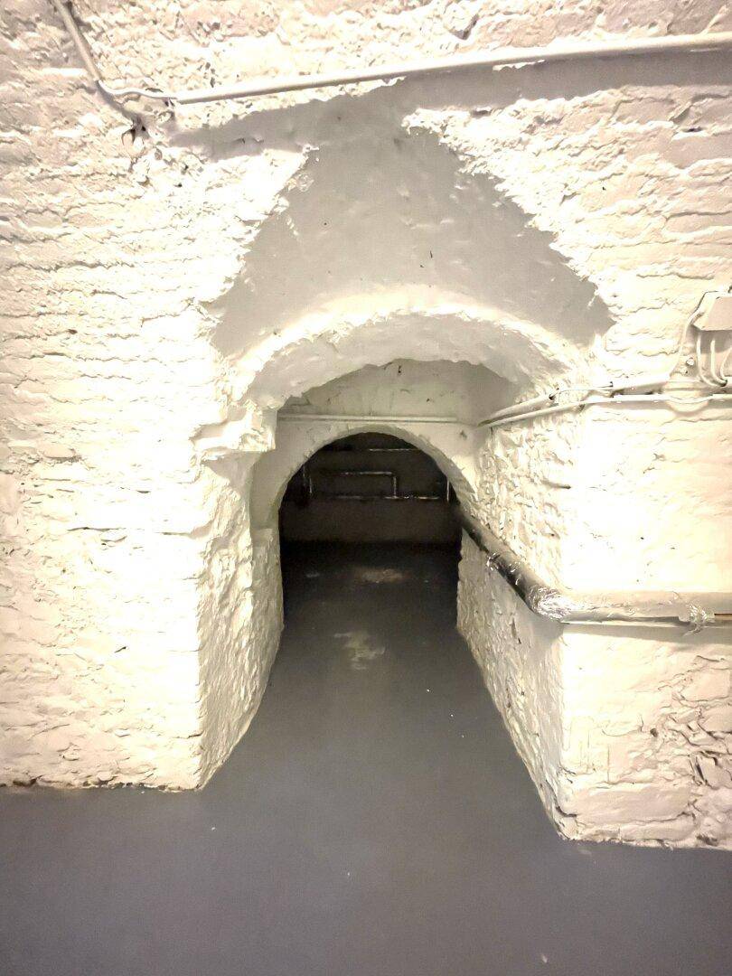 Historischer Gewölbekeller mit weiß gestrichenen Steinwänden und Durchgang zu weiteren Räumen.