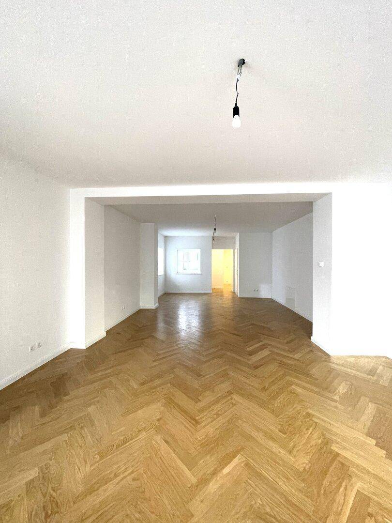 Geräumiger, leerer Wohnbereich mit Fischgrätparkett und weißen Wänden, bereit zur Einrichtung.