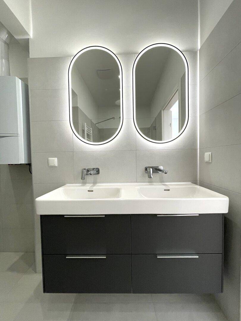 Elegantes Badezimmer mit Doppelwaschbecken, beleuchteten Spiegeln und modernen Armaturen.