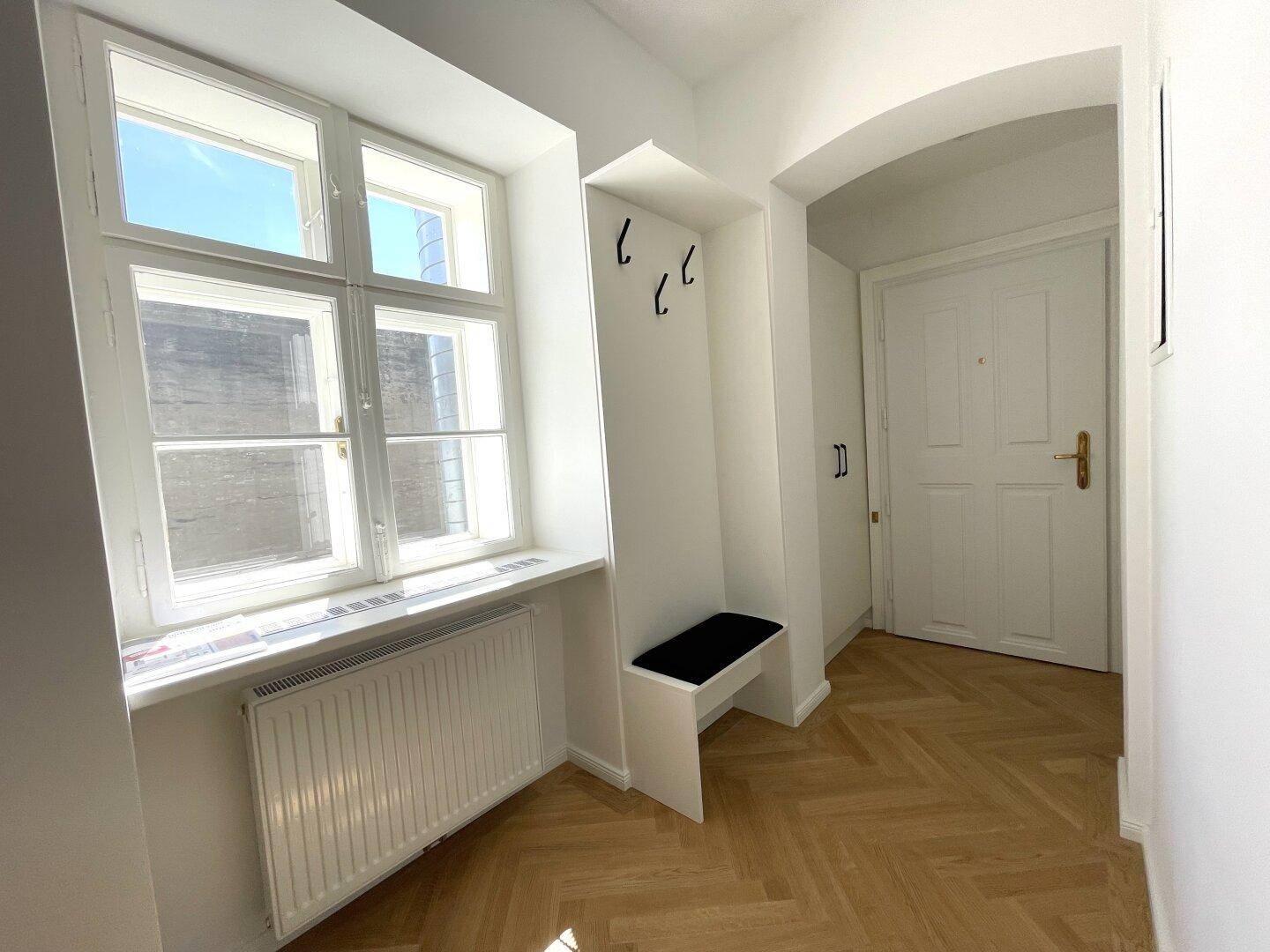 Heller Eingangsbereich mit Fischgrätparkett, Garderobennische und großem Fenster.