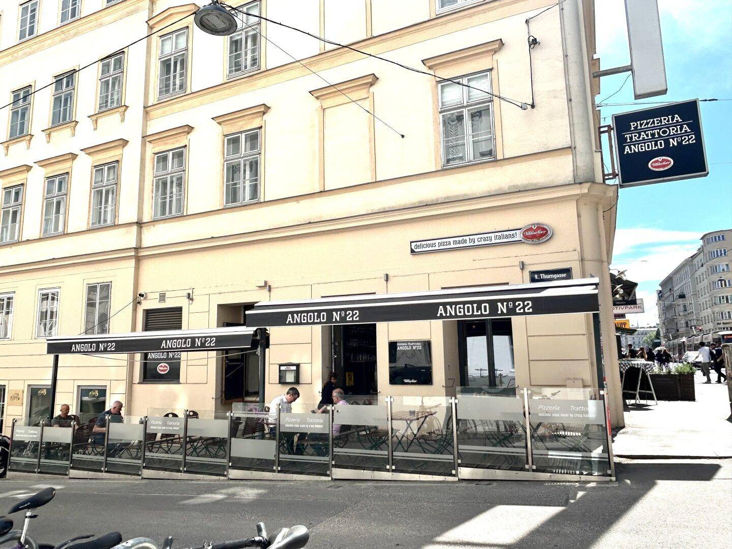 Nahaufnahme der Fassade eines Gebäudes mit einem Restaurant im Erdgeschoss und Außenbestuhlung.