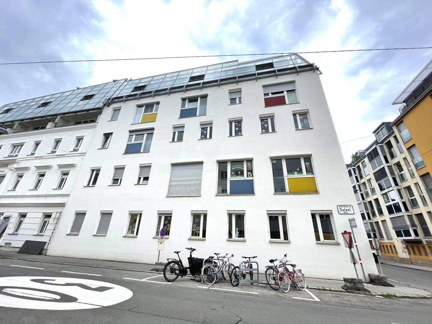 Moderne Gebäudefassade mit bunten Akzenten und vielen Fenstern, Fahrräder stehen davor auf der Straße.