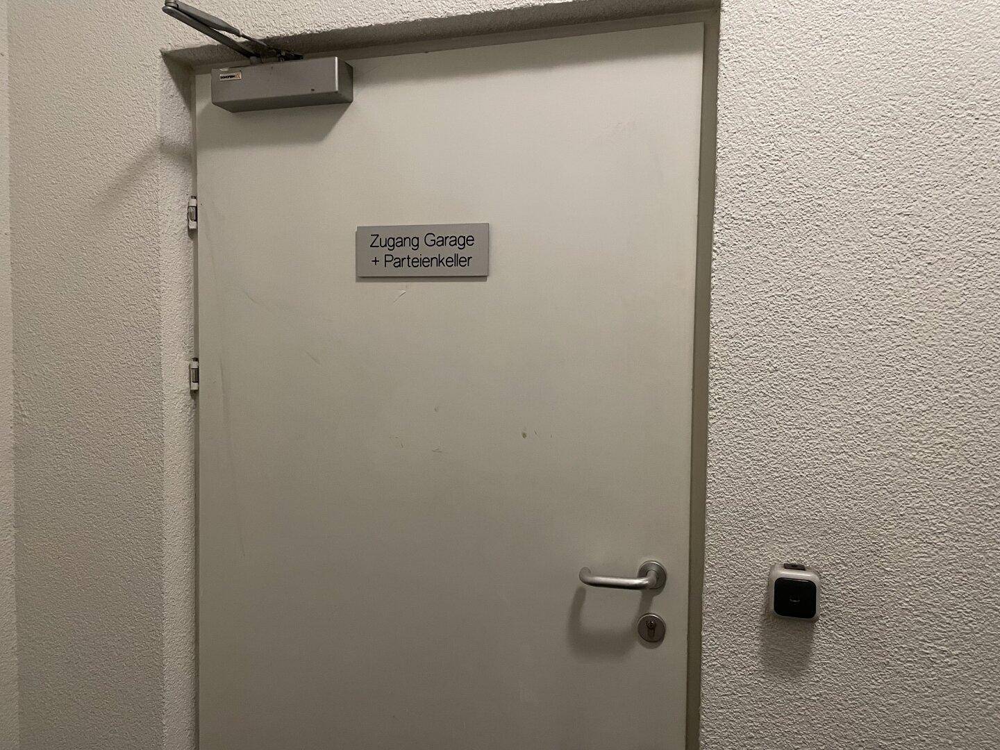 Eine Tür in einem Flur mit einem Schild, das den Zugang zur Garage und zum Parteienkeller anzeigt.