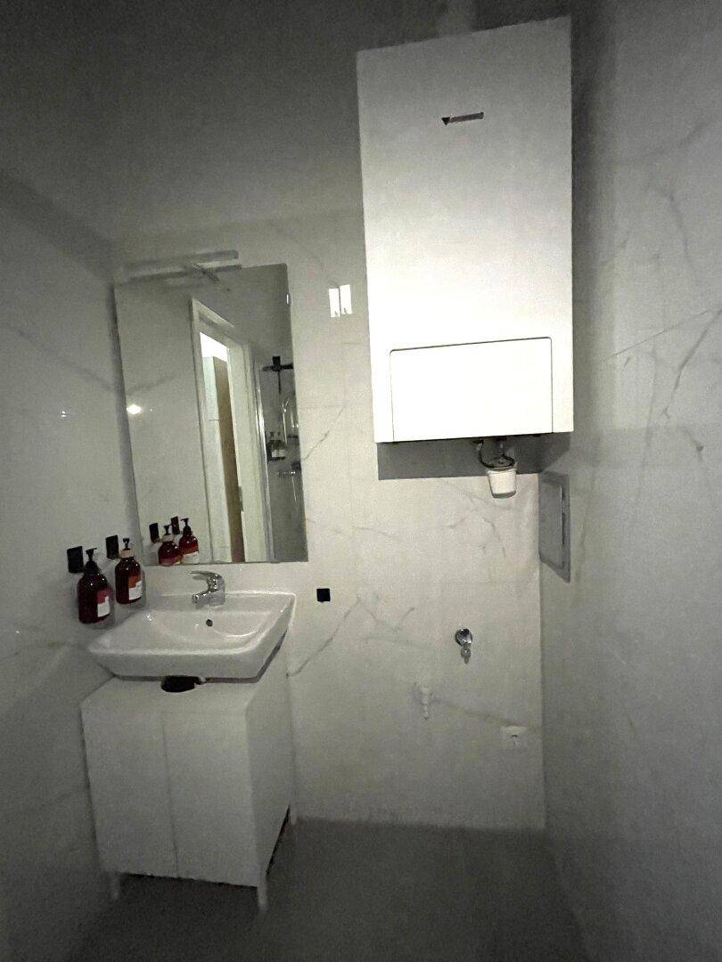 Modernes Badezimmer mit Waschbecken, Spiegel und Wandheizung, in hellen Marmorfliesen gehalten.