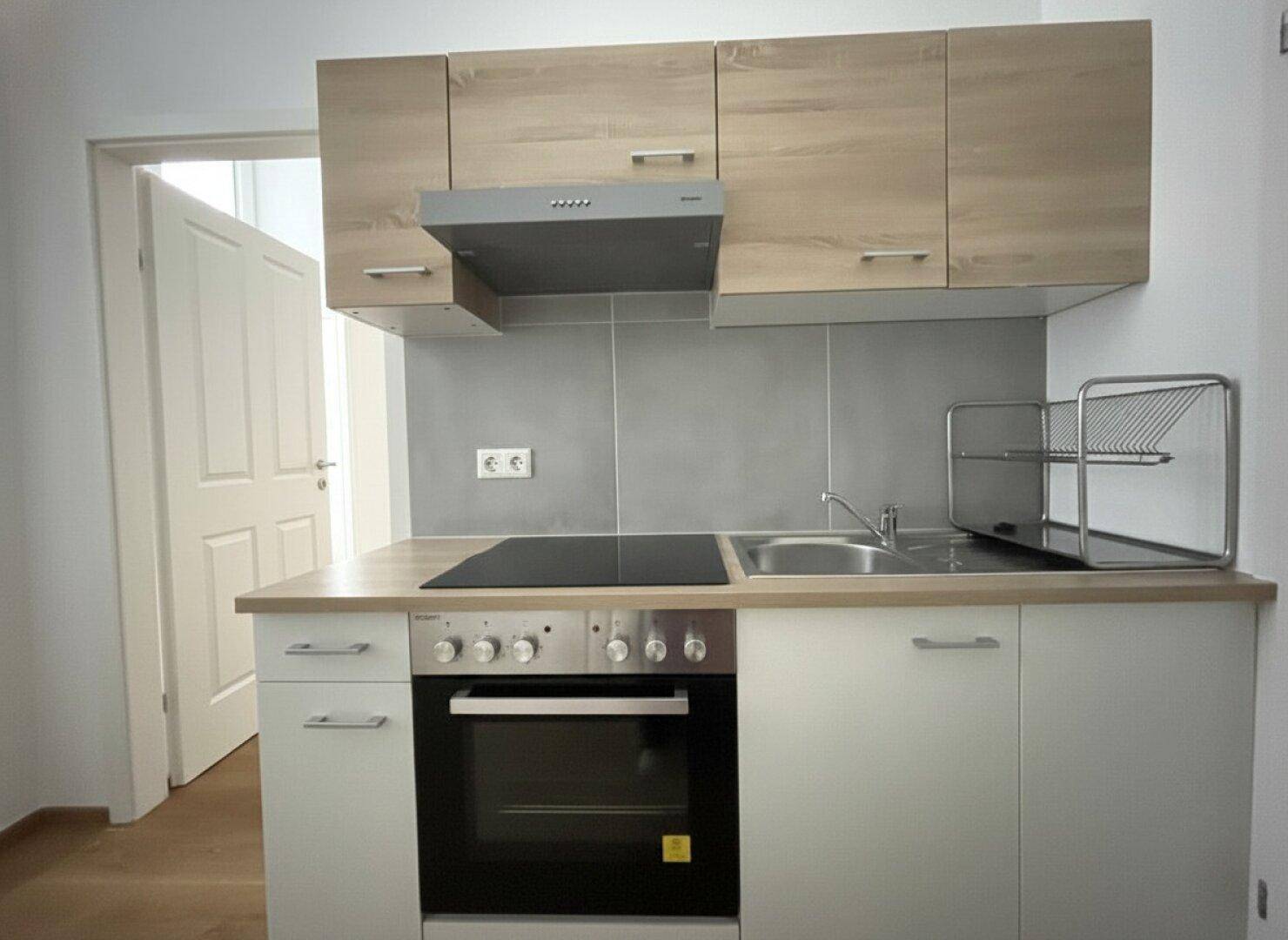 Detailansicht der modernen Küchenzeile mit Spüle, Kochfeld und Backofen, ideal für kleine Haushalte.