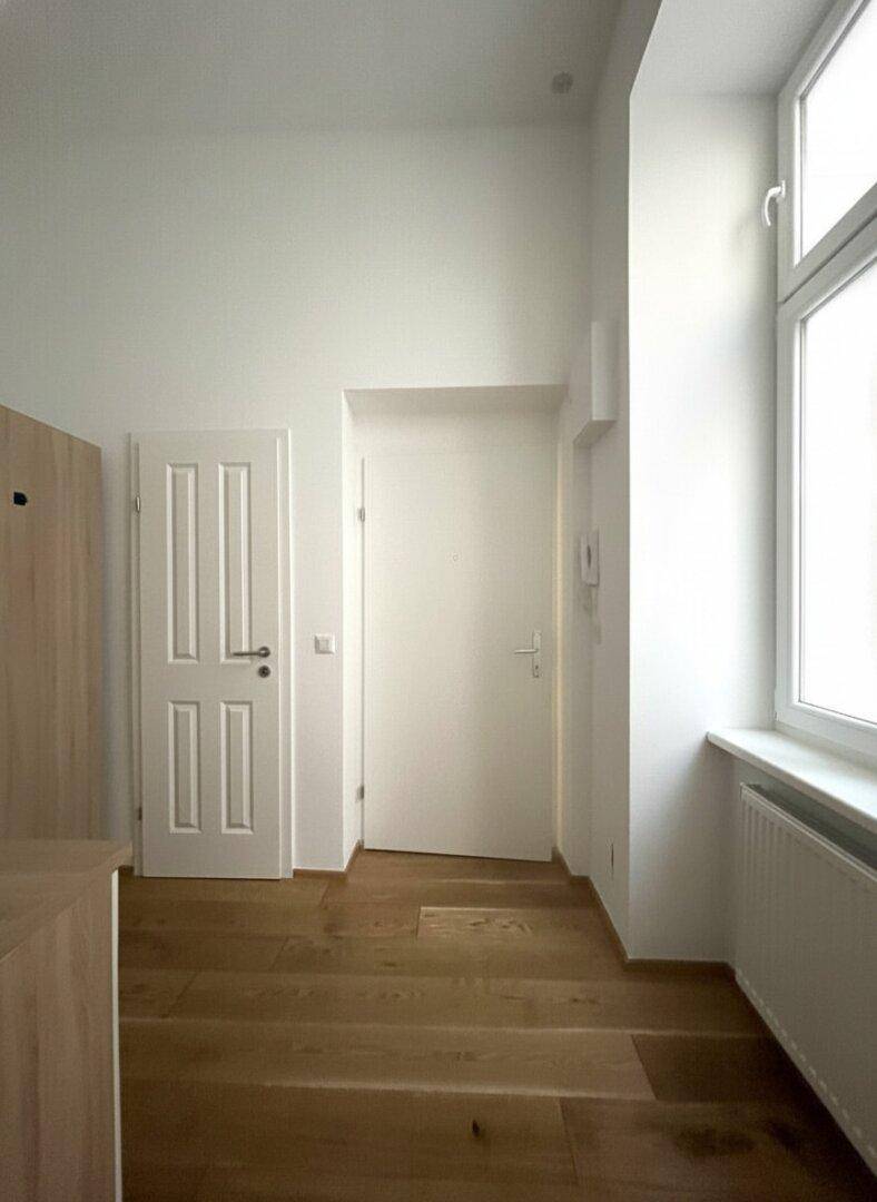Heller Flur mit Holzfußboden und einem Fenster, das Tageslicht in den Eingangsbereich bringt.