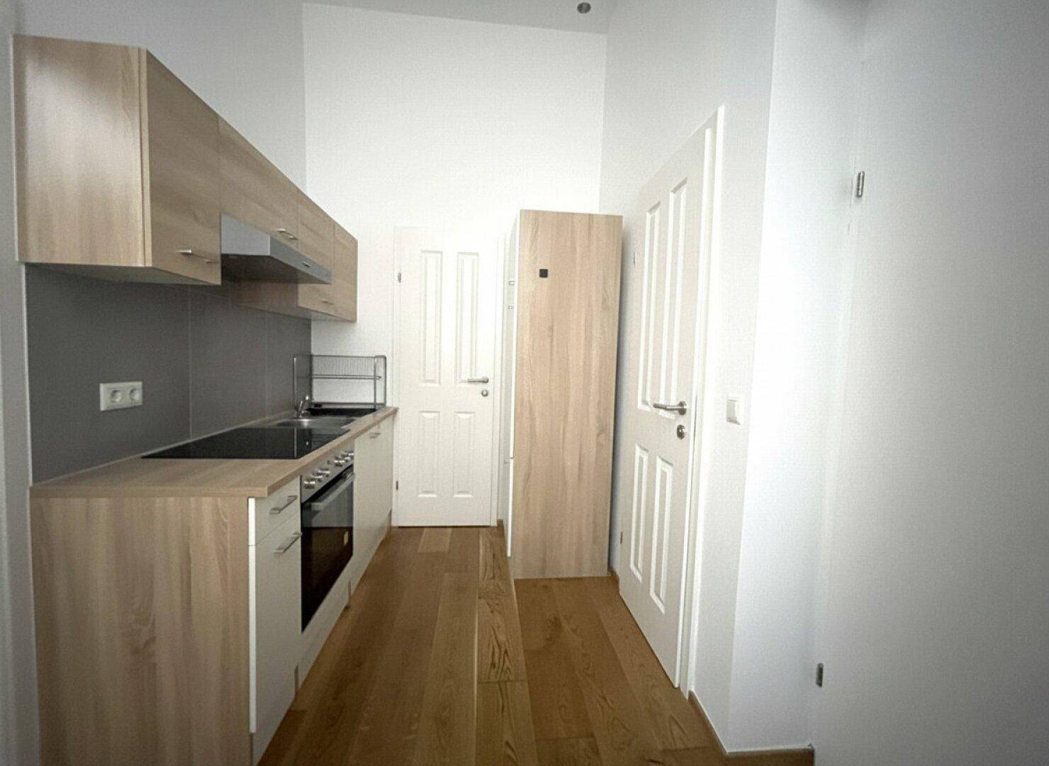 Moderne Küchenzeile mit hellen Holzschränken, integriertem Backofen und Kochfeld, sehr funktional.