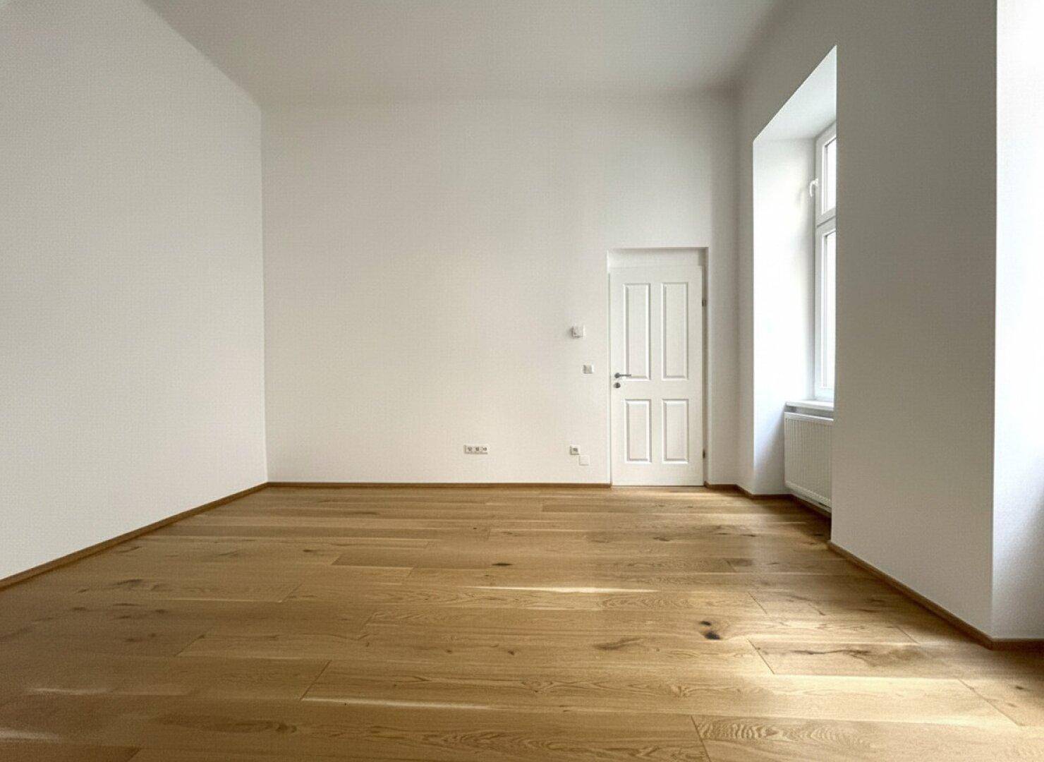 Geräumiges, helles Zimmer mit elegantem Holzfußboden und einem großen Fenster, ideal für Wohnzwecke.