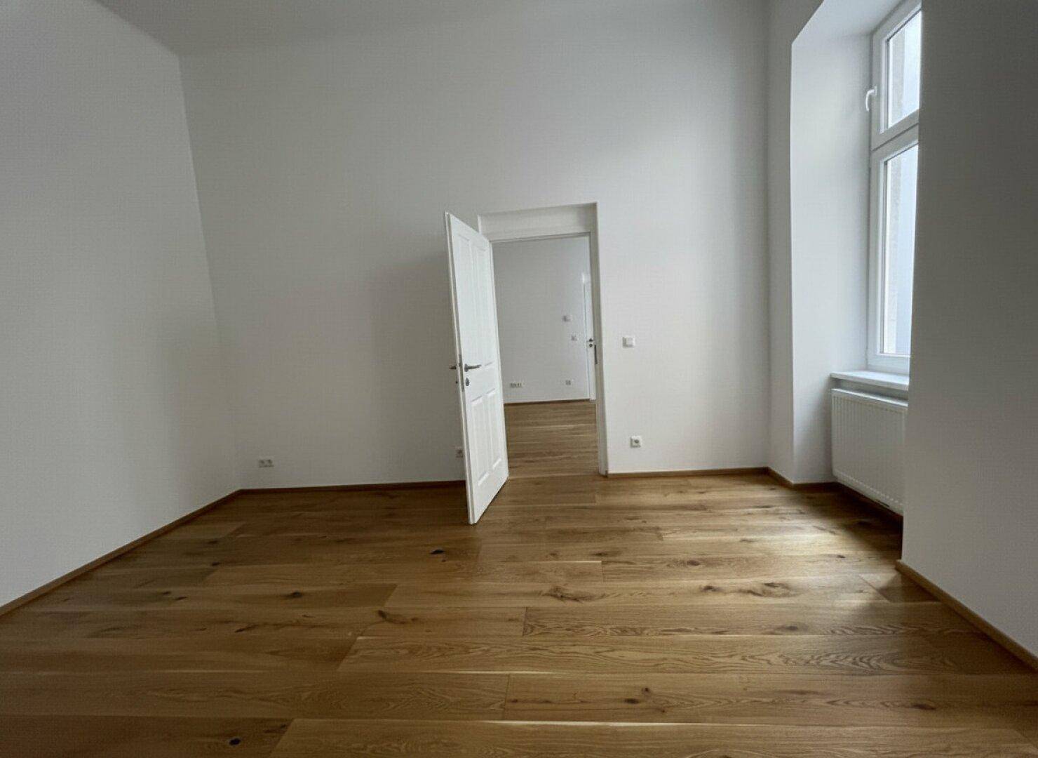 Helles Zimmer mit neuem Holzfußboden und einem Fenster, das den Blick nach draußen freigibt.