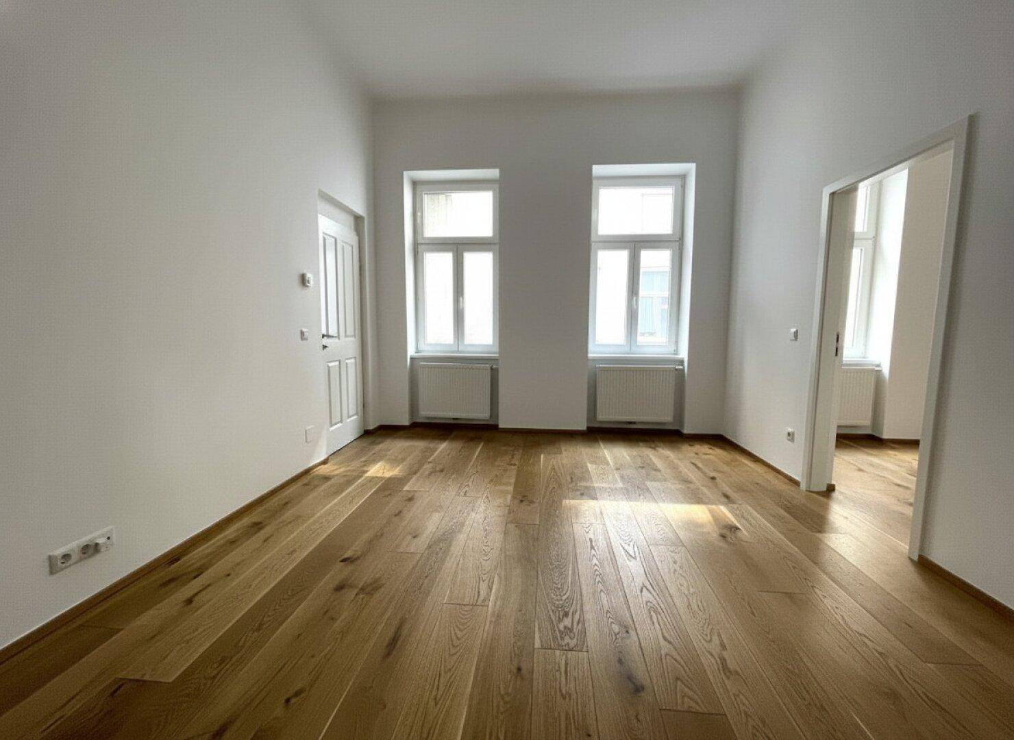 Heller Raum mit Holzboden und zwei Fenstern, bietet eine angenehme Wohnatmosphäre.