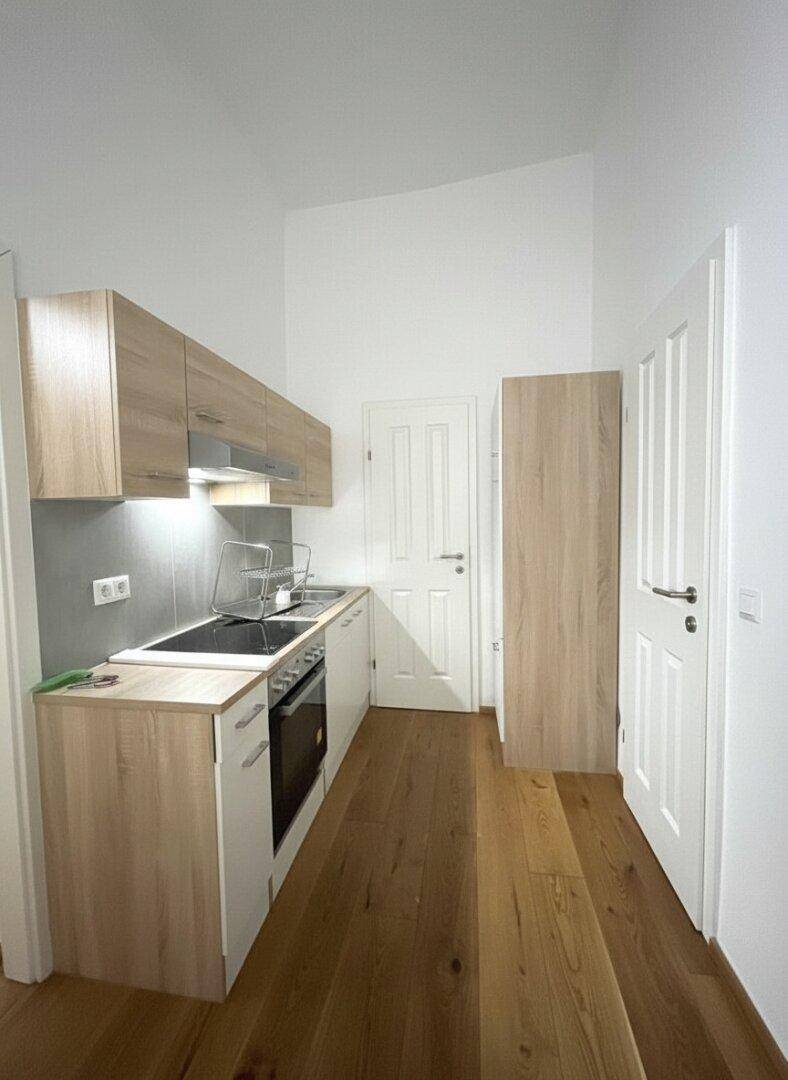 Kleine, funktionale Küchenzeile mit Holzoptik-Schränken und integrierten Geräten.