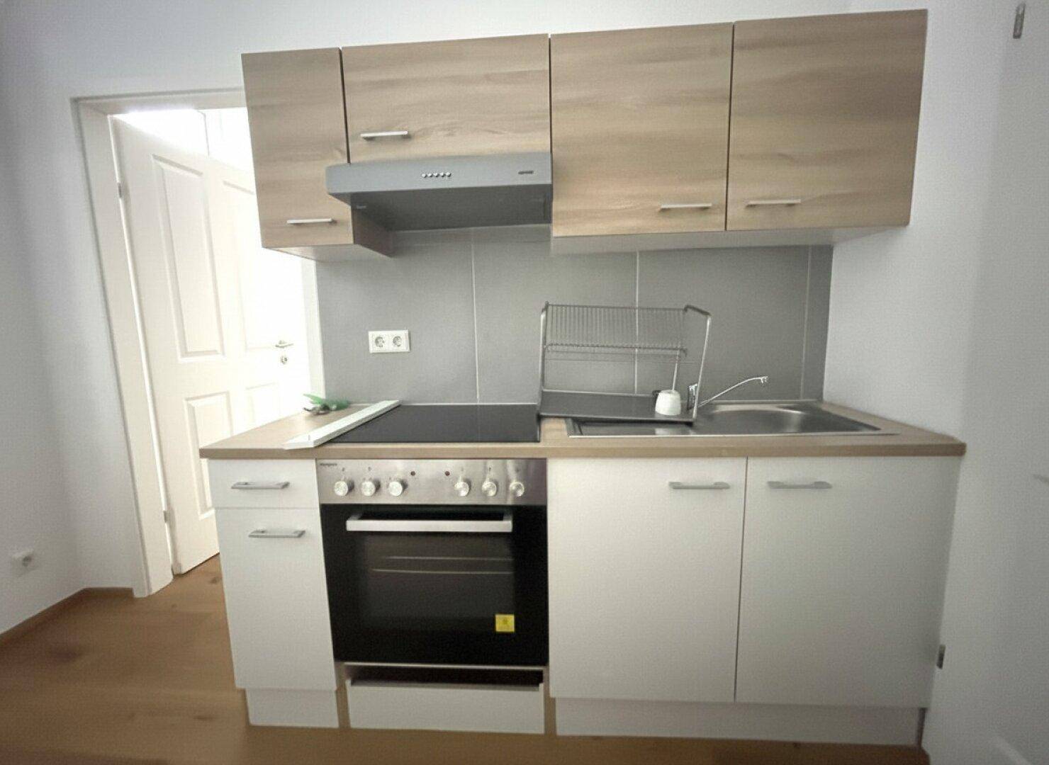 Kompakte Küchenzeile mit hellen Holzschränken, Kochfeld und Backofen, ideal für kleine Wohnungen.