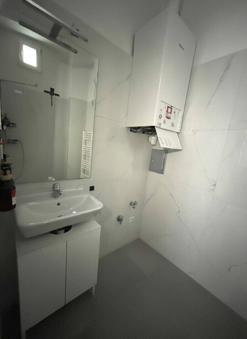 Modernes Badezimmer mit weißen Marmorfliesen, Waschbecken und Heiztherme an der Wand.
