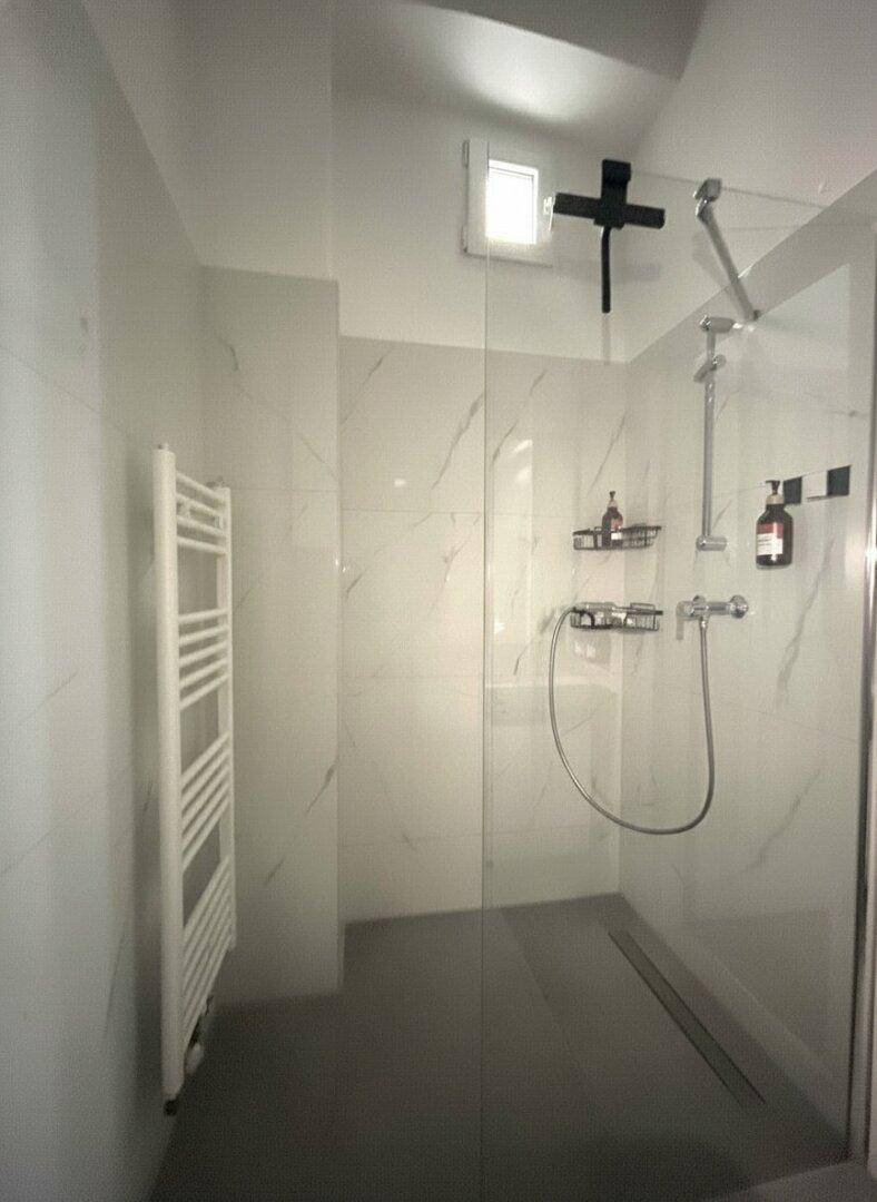 Zeitgemäße Dusche mit Glasabtrennung und weißen Marmorfliesen, inklusive Handtuchheizkörper.